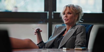 Movie still from “Yellowstone” (2018), created by John Linson – A woman sitting at a table with a cigarette in her mouth; Medium shot, Low angle