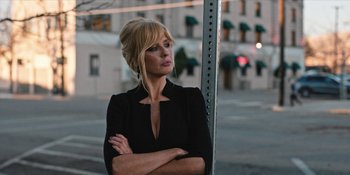 Movie still from “Yellowstone” (2018), created by John Linson – A woman standing on a sidewalk with her arms crossed; Close Up shot, Low angle