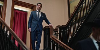 Movie still from “Yellowstone” (2018), created by John Linson – A man in a suit and tie walking up a staircase; Wide shot, Low angle