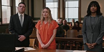 Movie still from “Yellowstone” (2018), created by John Linson – A woman in an orange prison uniform standing in front of a group of people; Medium shot, Over the shoulder angle