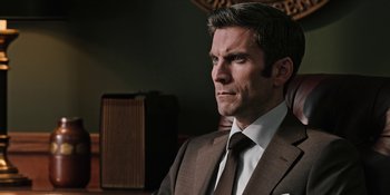 Movie still from “Yellowstone” (2018), created by John Linson – A man in a brown suit and white tie; Close Up shot, Over the shoulder angle