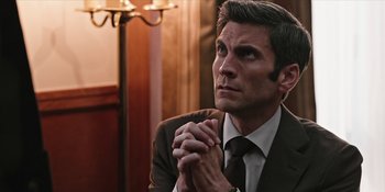 Movie still from “Yellowstone” (2018), created by John Linson – A person wearing a suit and tie; Close Up shot, High angle