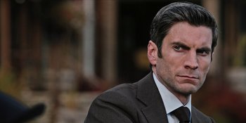 Movie still from “Yellowstone” (2018), created by John Linson – A person wearing a suit and tie; Close Up shot, Over the shoulder angle