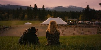 Movie still from “Yellowstone” (2018), created by John Linson – Two people sitting in the grass near a tent; Wide shot, High angle