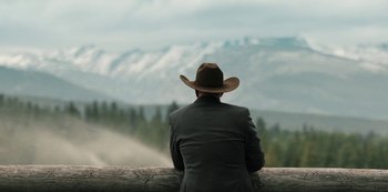 Movie still from “Yellowstone” (2018), created by John Linson – A man wearing a cowboy hat sitting on top of a wooden fence; Medium shot, Over the shoulder angle
