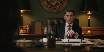 Movie still from “Yellowstone” (2018), created by John Linson – A man sitting at a desk in front of papers; Medium shot, Low angle