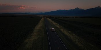 Movie still from “Yellowstone” (2018), created by John Linson – A car driving down a road in the middle of a field; Extreme Wide shot, High angle