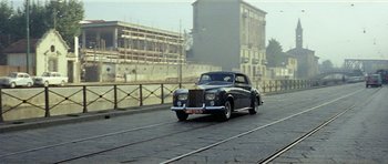 Movie still from “Yesterday, Today and Tomorrow” (1963), directed by Vittorio De Sica – An old car is driving down the street; Wide shot, Low angle