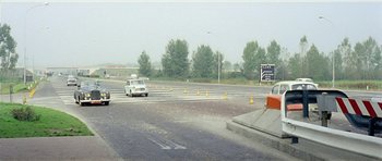 Movie still from “Yesterday, Today and Tomorrow” (1963), directed by Vittorio De Sica – A car driving down a street near a street sign; Extreme Wide shot, High angle