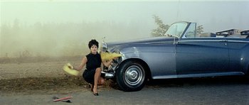 Movie still from “Yesterday, Today and Tomorrow” (1963), directed by Vittorio De Sica – A woman kneeling down next to a parked car; Wide shot, High angle