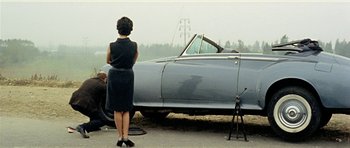 Movie still from “Yesterday, Today and Tomorrow” (1963), directed by Vittorio De Sica – A woman standing next to a car on the side of the road; Wide shot, High angle