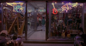 Movie still from “Yi Yi” (2000), directed by Edward Yang – A person walking in front of a store with guitars; Wide shot, High angle