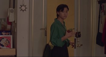 Movie still from “Yi Yi” (2000), directed by Edward Yang – A woman standing in front of a door holding a camera; Medium shot, Over the shoulder angle