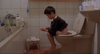 Movie still from “Yi Yi” (2000), directed by Edward Yang – A boy sitting on a toilet in a bathroom; Wide shot, High angle