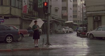 Movie still from “Yi Yi” (2000), directed by Edward Yang – A woman holding an umbrella while standing on the side of the street; Extreme Wide shot, High angle