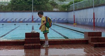 Movie still from “Yi Yi” (2000), directed by Edward Yang – A boy with a backpack standing next to a swimming pool; Wide shot, Low angle