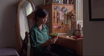 Movie still from “Yi Yi” (2000), directed by Edward Yang – A woman sitting in front of a desk holding a plant; Medium shot, High angle
