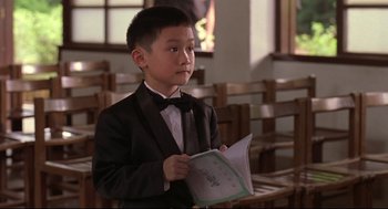 Movie still from “Yi Yi” (2000), directed by Edward Yang – A boy in a suit and bow tie holding papers; Medium shot, Over the shoulder angle