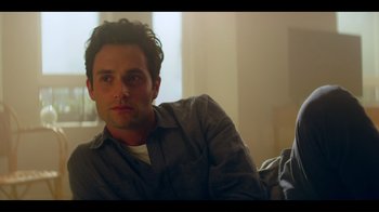 Movie still from “You” (2018), created by Sera Gamble – A person sitting on a couch; Close Up shot, Over the shoulder angle