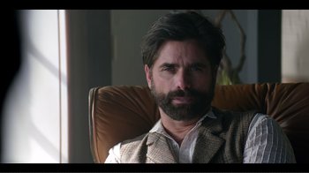 Movie still from “You” (2018), created by Sera Gamble – A man sitting in a chair wearing a suit and tie; Close Up shot, Over the shoulder angle