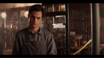 Movie still from “You” (2018), created by Sera Gamble – A man standing in front of a bookshelf in a room; Medium shot, Over the shoulder angle