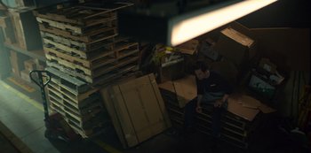 Movie still from “You” (2018), created by Sera Gamble – A man sitting on top of a pile of pallets; Wide shot, High angle