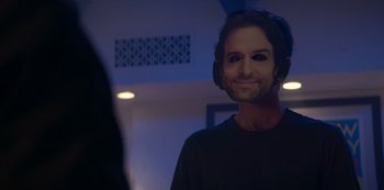 Movie still from “You” (2018), created by Sera Gamble – A man with headphones and a beard is smiling for the camera; Close Up shot, Over the shoulder angle