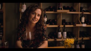 Movie still from “You” (2018), created by Sera Gamble – A woman sitting at a table with a glass of red wine; Close Up shot, Over the shoulder angle