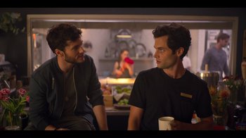 Movie still from “You” (2018), created by Sera Gamble – Two men are sitting in a kitchen talking to each other; Medium shot, Over the shoulder angle