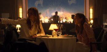 Movie still from “You” (2018), created by Sera Gamble – Two women sitting at a table in front of a bar; Medium shot, Over the shoulder angle