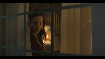 Movie still from “You” (2018), created by Sera Gamble – A woman looking out a window at night; Medium shot, Over the shoulder angle