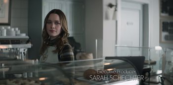 Movie still from “You” (2018), created by Sera Gamble – A woman in plaid shirt standing in front of a counter; Medium shot, Over the shoulder angle