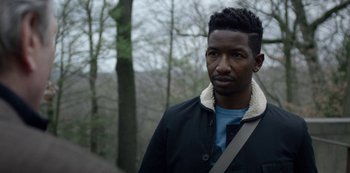 Movie still from “Archive 81” (2022), created by Rebecca Sonnenshine – A man standing in front of some trees; Close Up shot, Over the shoulder angle