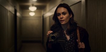 Movie still from “Archive 81” (2022), created by Rebecca Sonnenshine – A woman is holding a video camera in a hallway; Close Up shot, Over the shoulder angle