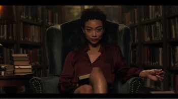 Movie still from “You” (2018), created by Sera Gamble – A woman sitting in a chair holding a book in her lap; Medium shot, High angle