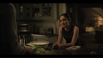 Movie still from “You” (2018), created by Sera Gamble – A woman sitting at a table with a bowl of vegetables; Medium shot, Over the shoulder angle