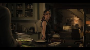 Movie still from “You” (2018), created by Sera Gamble – A woman standing at a table in a dark kitchen; Medium shot, Over the shoulder angle