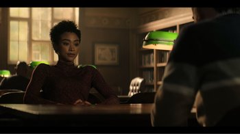 Movie still from “You” (2018), created by Sera Gamble – A woman sitting at a table in front of a bookshelf; Medium shot, Over the shoulder angle