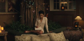 Movie still from “You” (2018), created by Sera Gamble – A woman sitting on the ground writing on a piece of paper; Medium shot, High angle