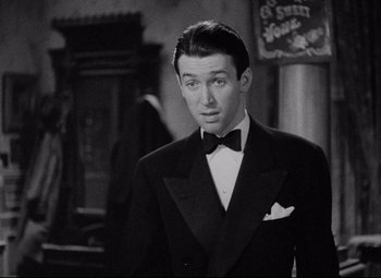 Movie still from “You Can't Take It with You” (1938), directed by Frank Capra – A man in a suit and bow tie standing next to a building; Close Up shot, Over the shoulder angle