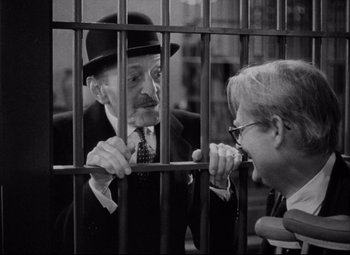 Movie still from “You Can't Take It with You” (1938), directed by Frank Capra – A man in a suit and a man in a top hat looking at each other through a fence; Medium shot, Over the shoulder angle