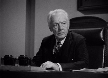 Movie still from “You Can't Take It with You” (1938), directed by Frank Capra – An older man sitting at a desk in a suit and tie; Medium shot, High angle