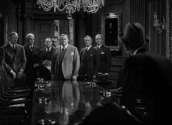 Movie still from “You Can't Take It with You” (1938), directed by Frank Capra – A black and white photo of a group of men standing around a conference table; Wide shot, High angle