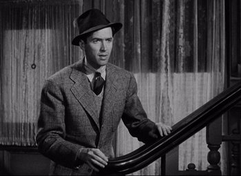 Movie still from “You Can't Take It with You” (1938), directed by Frank Capra – A man wearing a suit and a hat standing next to a railing; Medium shot, High angle