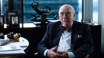 Movie still from “You've Got Mail” (1998), directed by Nora Ephron – An older man wearing a suit and bow tie sitting in front of a statue; Close Up shot, Over the shoulder angle