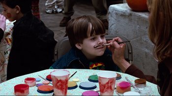Movie still from “You've Got Mail” (1998), directed by Nora Ephron – A child with a fake mustache is being painted; Medium shot, Over the shoulder angle