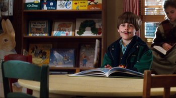 Movie still from “You've Got Mail” (1998), directed by Nora Ephron – A young boy sitting at a table with a book; Medium shot, Low angle