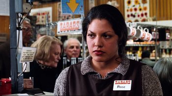 Movie still from “You've Got Mail” (1998), directed by Nora Ephron – A woman in a brown shirt is standing in front of other people; Close Up shot, Over the shoulder angle