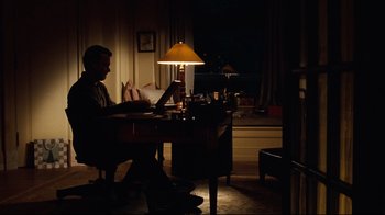 Movie still from “You've Got Mail” (1998), directed by Nora Ephron – A man sitting at a desk in a dark room; Wide shot, High angle
