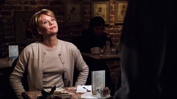 Movie still from “You've Got Mail” (1998), directed by Nora Ephron – A woman sitting at a table in front of a brick wall; Medium shot, Over the shoulder angle